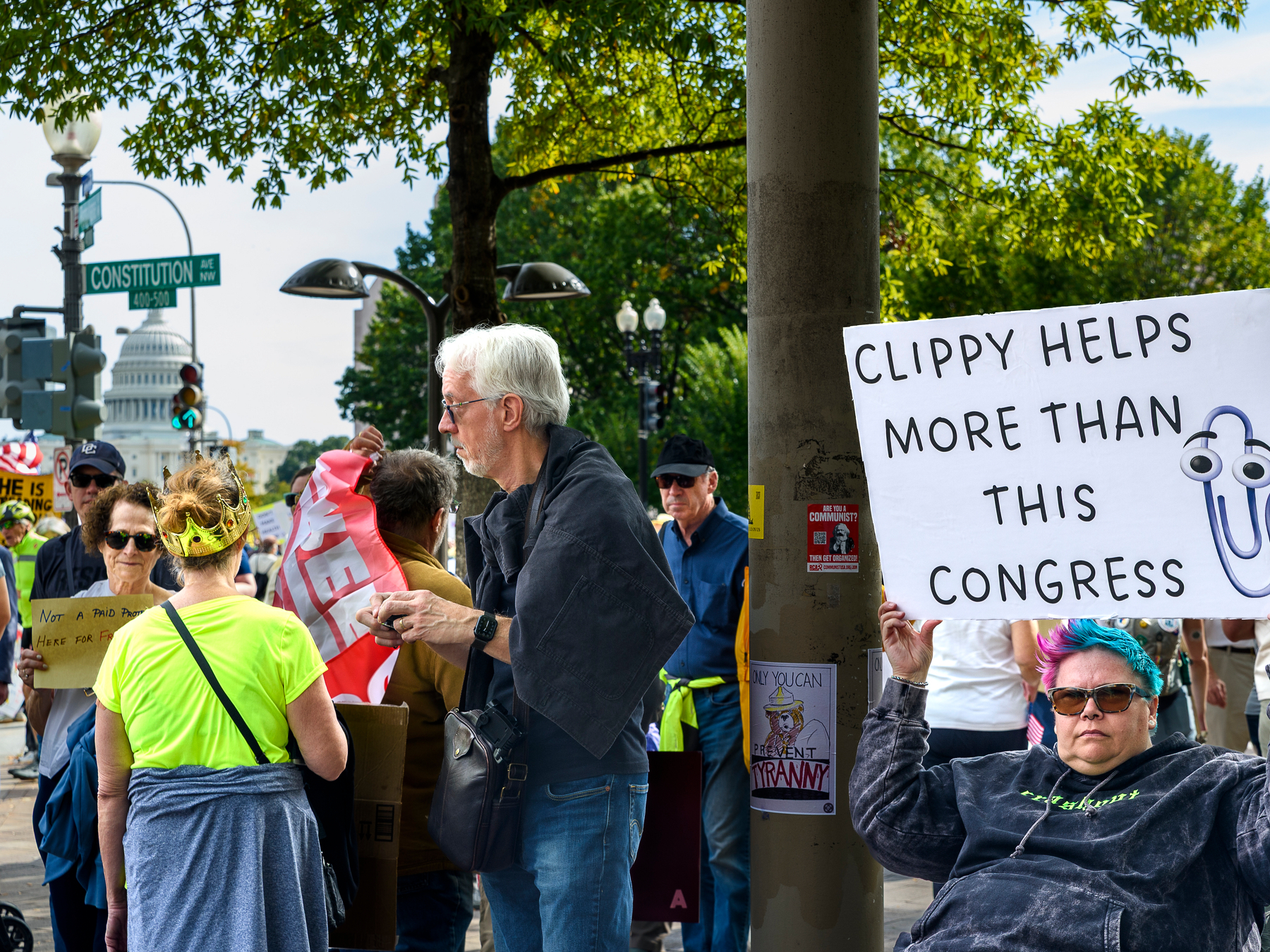A woman in a wheelchair holds up a sign that says 'Clippy helps more than this congress,' with a printed illustration of the infamous Microsoft Office software help agent.